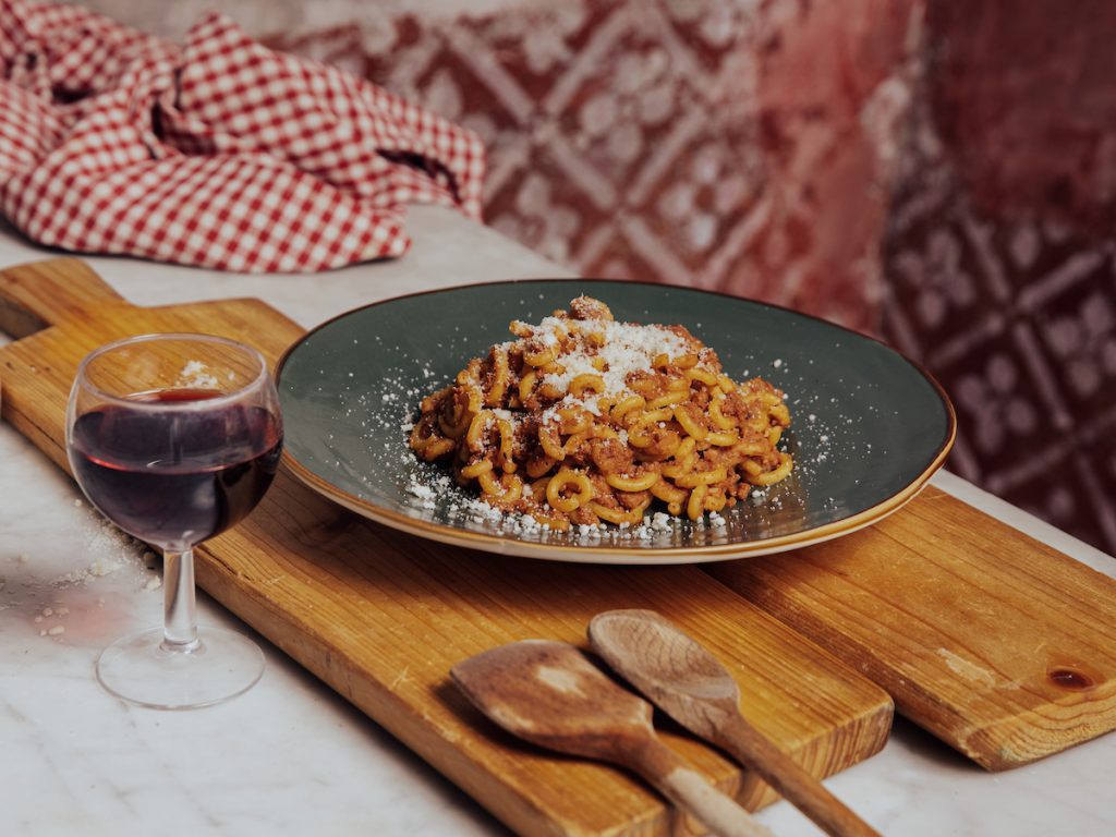 Foto di prodotti tipici emiliani: piatto di gramigna al ragù con un bicchiere di vino